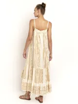 Vestido negro de breteles finos con escote en V y silueta amplia. Presenta un estampado geométrico en dorado que recorre paneles verticales y un ruedo con volado.