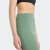 Calza deportiva de tiro alto, color verde salvia, ajustada al cuerpo y confeccionada en tejido elástico en 4 direcciones con tecnología de secado rápido. Posee bolsillos laterales.
