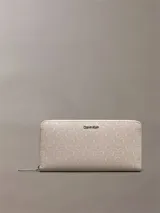 Billetera rectangular Calvin Klein con cierre perimetral de cremallera. Presenta un diseño texturizado con monograma de la marca en relieve y logo metálico en la parte frontal.