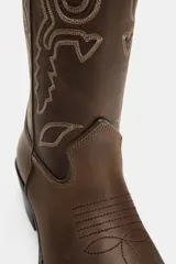 Bota estilo cowboy de piel con efecto desgastado. Presenta bordados decorativos en el cuerpo, doble tirador lateral y tacón medio con acabado en punta.