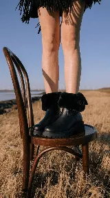 Bota de cuero vacuno color negro con interior forrado en corderito sintético. Presenta una caña media con borde superior de piel sintética, suela de goma tipo track con plataforma y punta redonda.