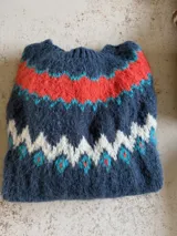 Sweater de punto tejido a mano en mohair, con diseño de canesú estampado en tonos azul, rojo, blanco y turquesa. Presenta cuello redondo y mangas largas.