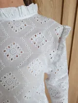 Blusa blanca de manga larga con cuello alto y volados en cuello y hombros.