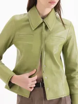 Chaqueta de cuero ovino color verde, de calce levemente entallado, cuello camisero clásico, mangas largas con puño, cierre frontal con broches a presión ocultos y dos bolsillos en la zona del busto.