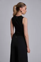 Remera sin mangas negra, ajustada al cuerpo, con cuello redondo y detalles de tachas metálicas plateadas a lo largo de los hombros y sisas.