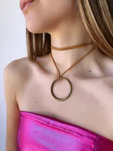 Colgante tipo choker con cordón de gamuza marrón y dije circular de metal en tono bronce envejecido.