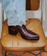 Bota estilo tejano de cuero color bordó con acabado brillante, taco cuadrado y punta cuadrada. Presenta costuras decorativas en el empeine y caña media.