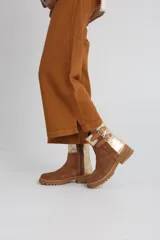 Bota estilo biker de caña media, confeccionada en cuero negro con detalles en gamuza marrón. Presenta correas ajustables con hebillas metálicas, tachas decorativas y suela track dentada.