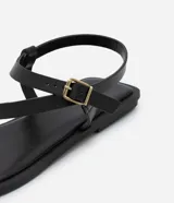 Sandalias planas de cuero sintético negro, con puntera cuadrada, tira delantera con dedera y tira trasera con hebilla metálica dorada.
