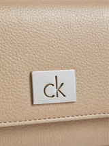 Billetera Calvin Klein trifold color beige con textura granulada y placa metálica con logo CK. Cuenta con múltiples compartimentos para tarjetas, billetes y documentos, protección RFID y bolsillo monedero.