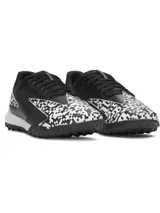 Championes de fútbol Under Armour Shadow Turf 3, diseñados para césped artificial. Presentan un diseño en color negro con detalles estampados en blanco y negro tipo pixelado. Cuentan con entresuela Charged Cushioning para absorción de impactos y suela de goma con tacos estratégicos para máximo agarre.