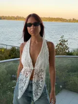 Top halter de encaje blanco con escote profundo y diseño de puntas asimétricas en el frente. Presenta un estilo delicado con transparencias y cierre frontal sutil.