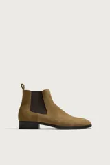 Bota Chelsea de gamuza color tostado, con paneles elásticos laterales en marrón oscuro, punta redonda y suela plana con pequeño tacón.