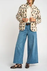 Campera de corderito con estampado floral en tonos tierra sobre base color crema. Presenta cuello redondo, cierre frontal con botones a presión y ribetes en color crema.