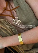 Pulsera dorada tipo brazalete rígido con perforaciones y pulsera dorada fina con dije de piedra blanca.