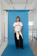 Remera de algodón blanca, con cuello redondo y mangas cortas. Presenta un estampado frontal con la palabra "KAPSUL" en rojo sobre un diseño floral en tono beige.