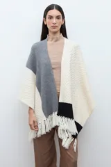 Ruana de tejido de punto con diseño color block en tonos crudo, gris y negro, con terminación de flecos en el ruedo y textura en relieve.