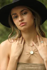 Collar con dije de sol dorado con centro de nácar, engarzado en un cordón fino color beige.