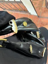 Cartera tipo baguette de gamuza color chocolate, con diseño decorado con diversos apliques metálicos, perlas y piezas de piedra. Cuenta con cierre superior y correa ajustable.