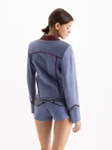 Chaqueta de gamuza color celeste con cuello camisero y detalles de ribetes en cuero marrón. Cuenta con cierre frontal y bolsillos aplicados con solapa.