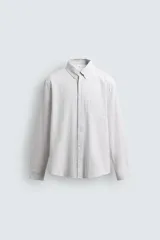Camisa de corte relajado confeccionada en tejido de algodón con textura, diseño a rayas verticales, cuello abotonado, manga larga con puños y bolsillo de plastrón en el pecho.