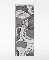 Chal jacquard de algodón orgánico con diseño estampado en tonos grises y blancos, logo de la marca y remates desflecados en los extremos.