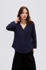 Blusa de viscosa color beige con cuello en V, cierre parcial de botones frontales, bolsillo en el pecho y mangas 3/4.