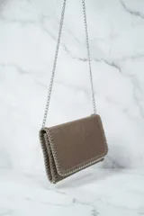 Cartera de hombro con solapa y bordes ribeteados con una cadena metálica entrelazada. Presenta un diseño tipo sobre con acabado texturizado y una correa de cadena larga.