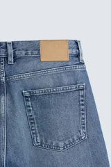 Pantalón de jean con corte recto desde la cadera y leve ensanchamiento en el bajo. Presenta tiro medio, cinco bolsillos, cierre frontal con cremallera y botón, y un acabado con efecto lavado.