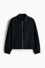 Campera negra de sarga de algodón, con cuello inglés, cierre frontal metálico y bolsillos delanteros ribeteados. Presenta elástico revestido en puños y bajo, y diseño forrado en su interior.