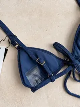 Top de bikini verde militar brillante, estilo triángulo, con argollas decorativas, bretel decorativo removible, forro y relleno removible. Los breteles son regulables y se ata en la espalda.