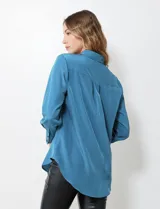 Camisa de satén color violeta, con cuello clásico, cierre frontal con botones, manga larga con puños anchos abotonados y bolsillo aplicado en el pecho.