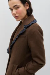 Tapado de lana color marrón con silueta entallada. Presenta solapas clásicas decoradas con un volado en contraste de color azul oscuro, cierre frontal con un botón y bolsillos laterales. Las mangas cuentan con detalles de botones en los puños.