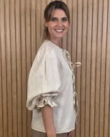 Camisa color beige de lino con mangas abullonadas tres cuartos y cierre frontal mediante múltiples lazos para atar.