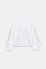 Camisa de color celeste con cuello subido, manga larga abullonada con puños elásticos y detalle de volantes en el cuello y a lo largo de la botonadura frontal.