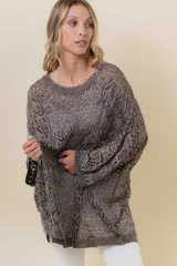 Buzo de tejido liviano y calado con brillo sutil, color gris oscuro o negro. Presenta un calce amplio y mangas amplias, con un detalle de tiras entrelazadas en la espalda. El largo es irregular, más largo en la parte trasera.