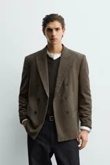 Blazer de corte relajado confeccionada en tejido con lana, con diseño de cuadros pequeños. Presenta cuello con solapas de pico, cierre frontal de botonadura cruzada, manga larga con botones en los puños y bolsillos de vivo en el pecho y la cadera.