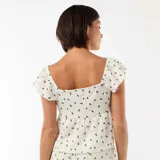 Top de tejido arrugado color blanco con estampado floral oscuro, escote cuadrado con pequeño lazo y recorte frontal, y mangas cortas con volados.
