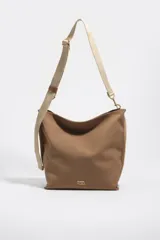 Bolso bandolera de tamaño mediano de la marca Bimba y Lola, color marrón, con exterior de nylon, correa ajustable de lona en tono tostado y detalles de metal dorado. Incluye cierre superior y el logo de la marca estampado en el frente.