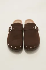 Suecos negros de estilo zueco con capellada de cuero sintético, detalle de hebilla metálica dorada y tachas decorativas alrededor de la suela. Poseen plantilla ergonómica y suela de plataforma dentada.