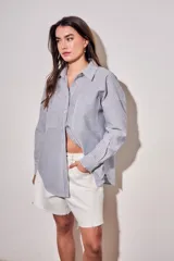 Camisa de corte oversize con diseño de rayas verticales en tonos azul y blanco. Presenta cuello clásico, cierre frontal con botones y mangas largas con puños abotonados.