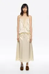 Falda midi de corte línea A en color beige, confeccionada en acetato. Presenta cremallera lateral invisible, bolsillos de plastrón y detalle de encaje a tono en el bajo.