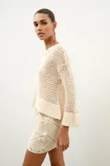 Minifalda de tiro medio confeccionada en ante color beige, decorada con aplicaciones de tejido tipo crochet blanco formando un patrón de rombos. Cuenta con cierre de cremallera oculta en la costura.