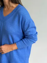 Sweater de tejido de punto color azul, con escote en V, manga larga con puños acanalados y diseño holgado con costura central vertical y ruedo asimétrico.