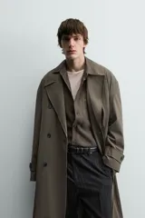 Trench color verde militar, de corte oversized, con cuello con solapas de muesca y manga larga con puño y trabilla. Presenta bolsillos de plastrón con solapa en la cadera y un bolsillo interior. Tiene una abertura en el centro de la espalda y cierre frontal de botonadura cruzada.