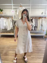 Vestido midi de lino color beige, corte recto, con escote en V y mangas cortas. Presenta aberturas laterales en el ruedo.