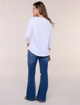 Remera blanca de algodón con elastano, de corte semi holgado, escote bote con ojalillos metálicos frontales, mangas tres cuartos raglán y ruedo asimétrico curvado.