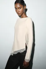 Top de manga larga en tejido suave color gris, con cuello redondo y bajo asimétrico decorado con encaje negro a tono. Presenta detalles de encaje negro en los puños.