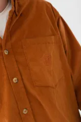 Camisa de pana azul marino de manga larga con cuello abotonado, cierre frontal con botones color hueso, bolsillo de parche en el pecho izquierdo y logo bordado en el bolsillo.