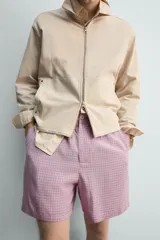 Bermuda de hombre con corte relaxed fit, tiro medio, cintura elástica con botón y cierre de cremallera. Presenta un patrón de cuadros pequeños en tonos rosados y grises.